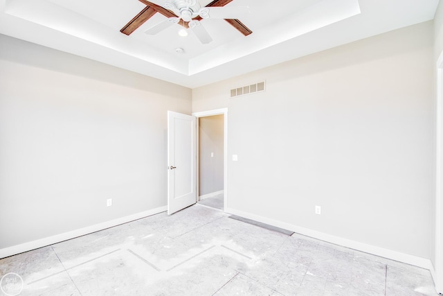 empty room with ceiling fan and a tray ceiling