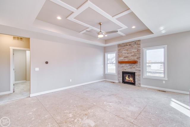 unfurnished living room featuring a raised ceiling, a stone fireplace, and ceiling fan