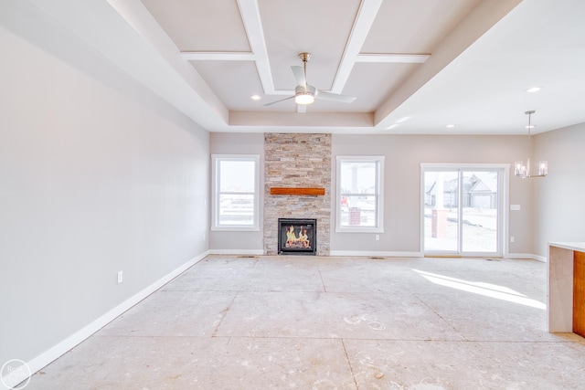 unfurnished living room featuring a healthy amount of sunlight, a stone fireplace, a raised ceiling, and ceiling fan with notable chandelier