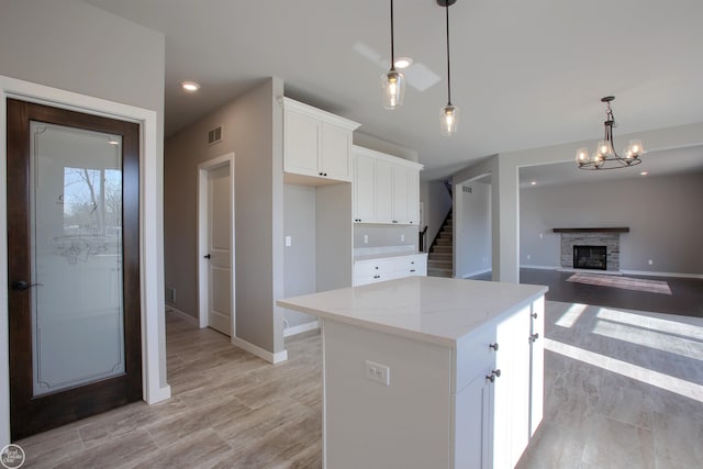 kitchen featuring a kitchen island, white cabinets, decorative light fixtures, a notable chandelier, and a stone fireplace