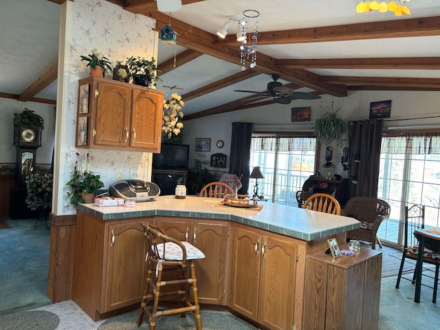 kitchen with ceiling fan, kitchen peninsula, light carpet, and vaulted ceiling with beams