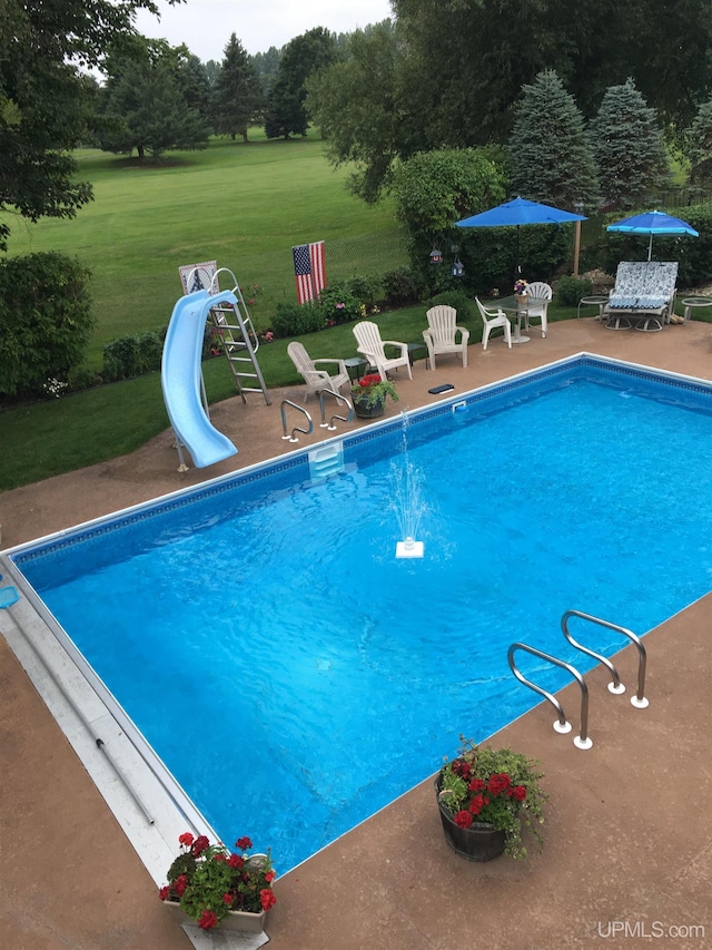 view of swimming pool featuring a lawn, a water slide, pool water feature, and a patio area