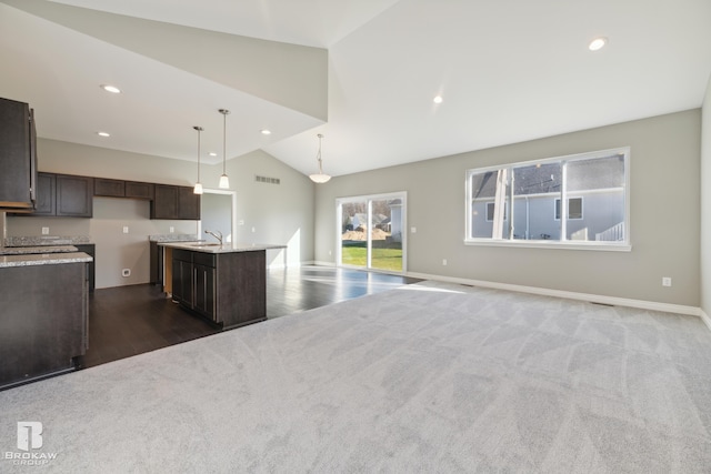 kitchen featuring light stone counters, dark carpet, a kitchen island with sink, high vaulted ceiling, and hanging light fixtures