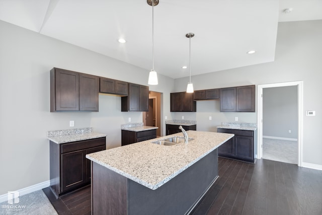 kitchen featuring an island with sink, decorative light fixtures, light stone countertops, dark hardwood / wood-style floors, and sink