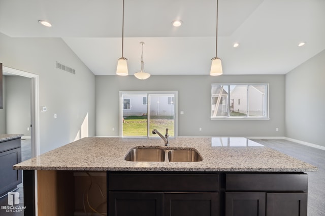 kitchen with light stone counters, lofted ceiling, decorative light fixtures, sink, and a center island with sink