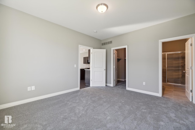 unfurnished bedroom featuring a walk in closet, dark carpet, and ensuite bath