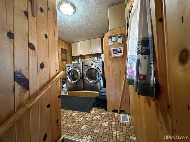 clothes washing area featuring wooden walls, cabinets, and separate washer and dryer