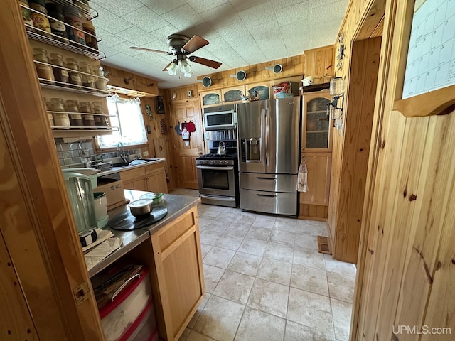 kitchen with wood walls, appliances with stainless steel finishes, light tile floors, ceiling fan, and sink