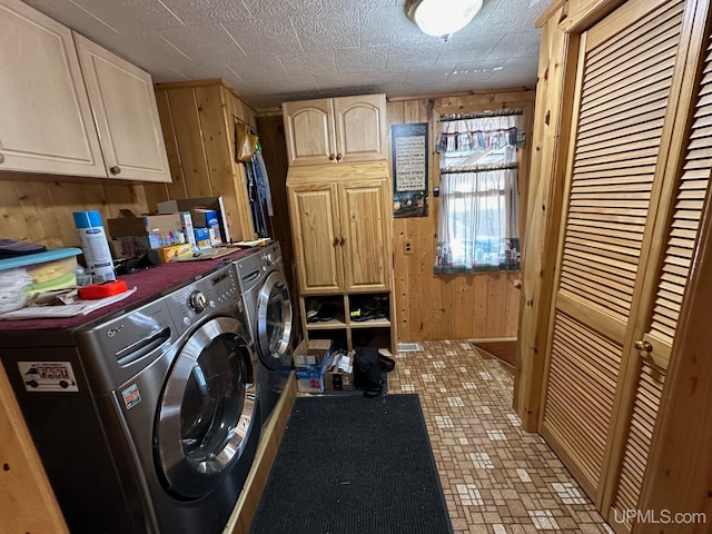 clothes washing area featuring washing machine and clothes dryer, wooden walls, cabinets, and light tile floors