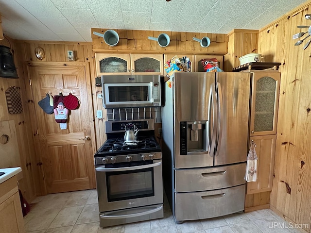 kitchen with wood walls, stainless steel appliances, and light tile floors