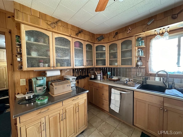 kitchen featuring ceiling fan, sink, light tile floors, stainless steel dishwasher, and wooden walls