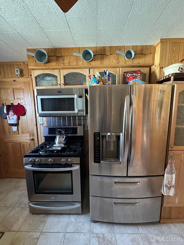 kitchen featuring wood walls, light tile flooring, and appliances with stainless steel finishes