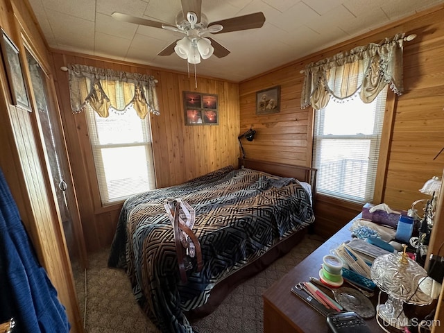 bedroom featuring wood walls, dark carpet, multiple windows, and ceiling fan