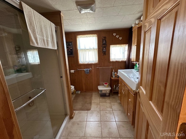 bathroom featuring tile flooring, a shower with shower door, wood walls, toilet, and vanity