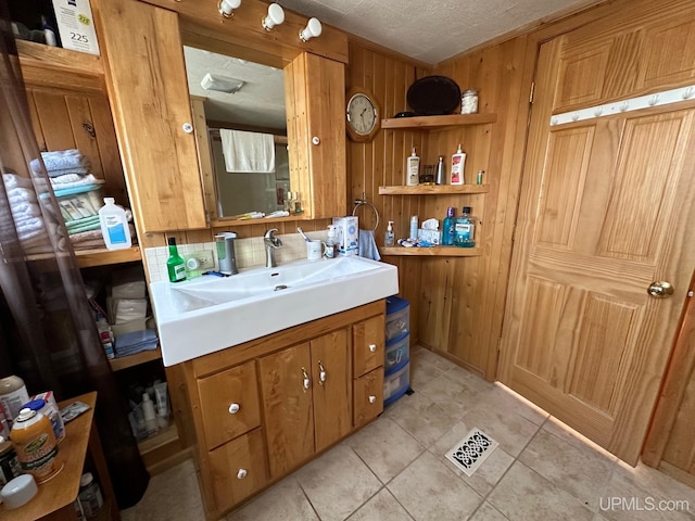 bathroom with wooden walls, tile floors, vanity, and a textured ceiling