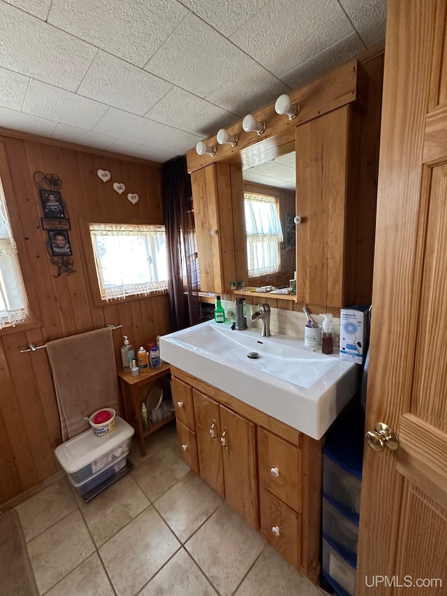 bathroom featuring tile flooring, wood walls, large vanity, and a wealth of natural light