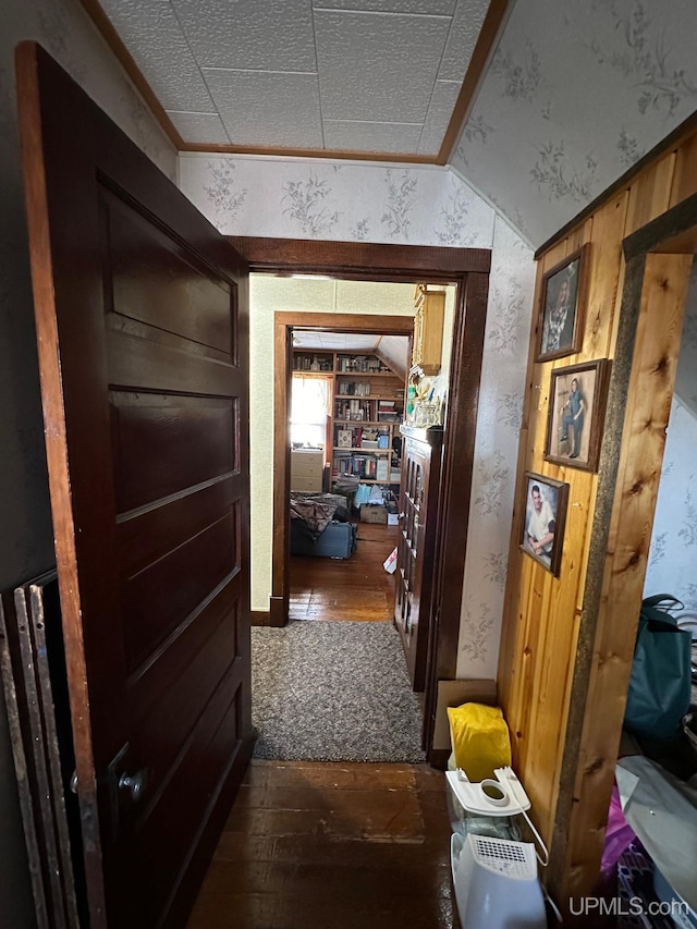 corridor with dark wood-type flooring, wooden walls, and vaulted ceiling