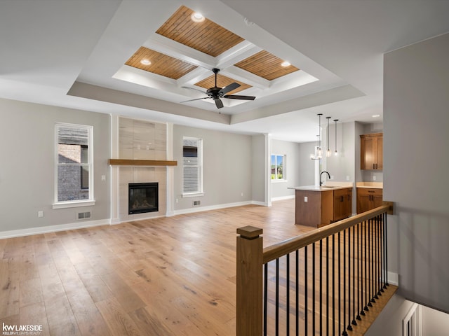 unfurnished living room with a tray ceiling, sink, coffered ceiling, and light wood-type flooring