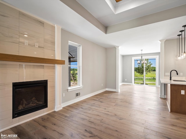 unfurnished living room featuring a tile fireplace, light wood-type flooring, a healthy amount of sunlight, and sink