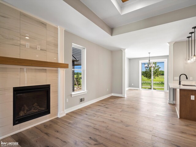 unfurnished living room featuring a tile fireplace, light wood-type flooring, a healthy amount of sunlight, and sink