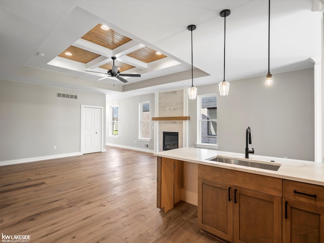 kitchen with sink, decorative light fixtures, light hardwood / wood-style floors, light stone counters, and kitchen peninsula