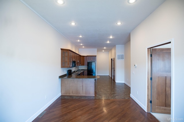 kitchen featuring dark stone counters, dark hardwood / wood-style floors, kitchen peninsula, black appliances, and sink