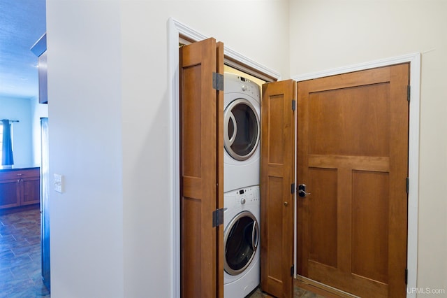 laundry area featuring dark tile floors and stacked washing maching and dryer