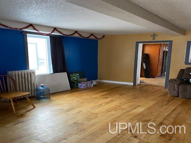 empty room featuring light hardwood / wood-style flooring, a textured ceiling, and radiator