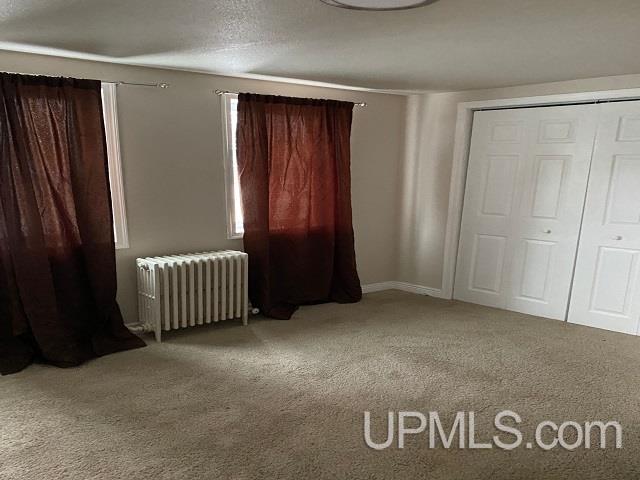 unfurnished bedroom featuring a closet, radiator heating unit, and carpet