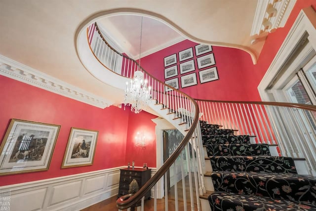 staircase featuring a notable chandelier, ornamental molding, hardwood / wood-style flooring, and a towering ceiling