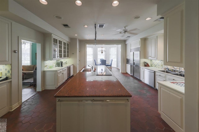 kitchen with tasteful backsplash, an island with sink, ceiling fan, stainless steel appliances, and dark tile floors