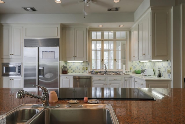 kitchen with white cabinets, tasteful backsplash, ceiling fan, and built in appliances