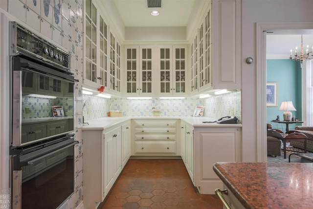 kitchen featuring black double oven, backsplash, dark tile floors, and a chandelier