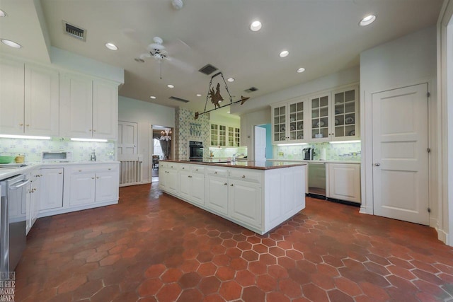 kitchen with a large fireplace, ceiling fan, tasteful backsplash, dark tile flooring, and white cabinets