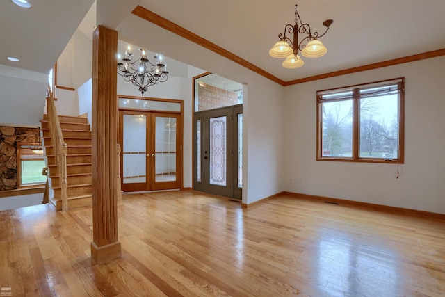 empty room with ornamental molding, french doors, an inviting chandelier, and light hardwood / wood-style flooring