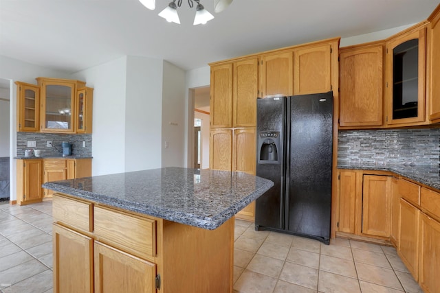 kitchen featuring light tile floors, dark stone countertops, backsplash, a kitchen island, and black refrigerator with ice dispenser