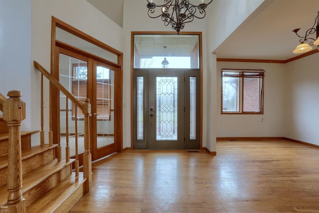 entrance foyer with ornamental molding, french doors, a chandelier, and light hardwood / wood-style flooring