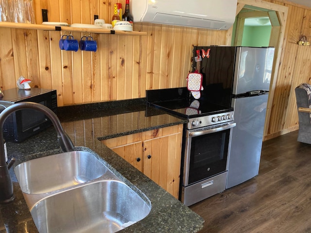 kitchen with wood walls, appliances with stainless steel finishes, dark stone counters, and sink