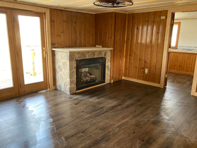 unfurnished living room with a stone fireplace, wooden walls, and dark hardwood / wood-style floors