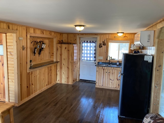 kitchen with sink, dark wood-type flooring, wood walls, and black refrigerator