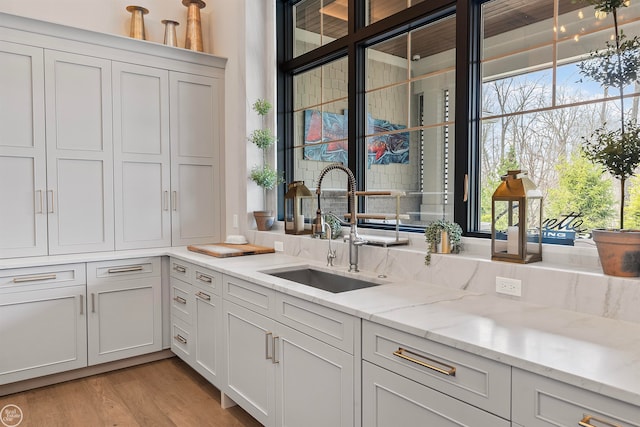 kitchen with sink, white cabinets, light stone counters, and light hardwood / wood-style flooring