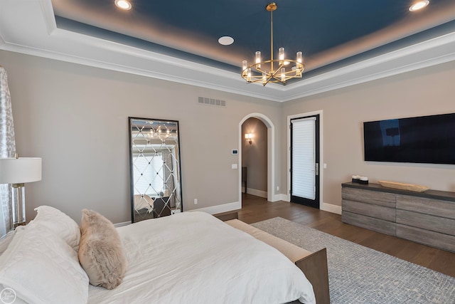 bedroom with a chandelier, dark wood-type flooring, and a raised ceiling