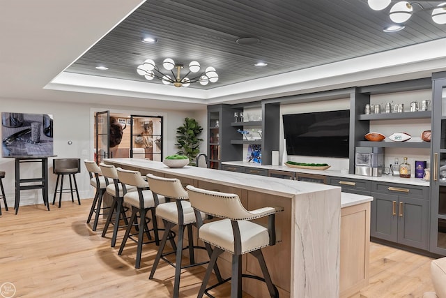 bar featuring light stone countertops, light wood-type flooring, an inviting chandelier, wooden ceiling, and a raised ceiling