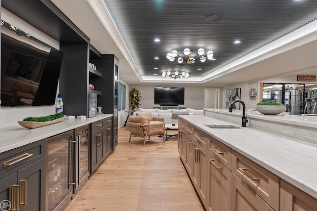 kitchen with light stone countertops, a tray ceiling, light hardwood / wood-style floors, sink, and a chandelier