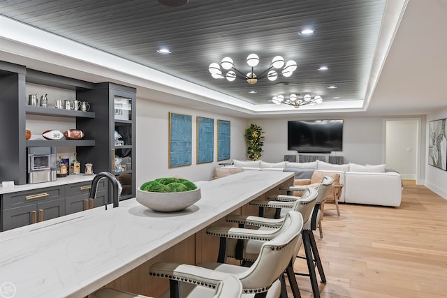 kitchen featuring a kitchen breakfast bar, light wood-type flooring, a raised ceiling, light stone counters, and gray cabinetry