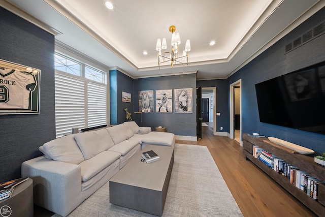 living room with a chandelier, light wood-type flooring, and a raised ceiling