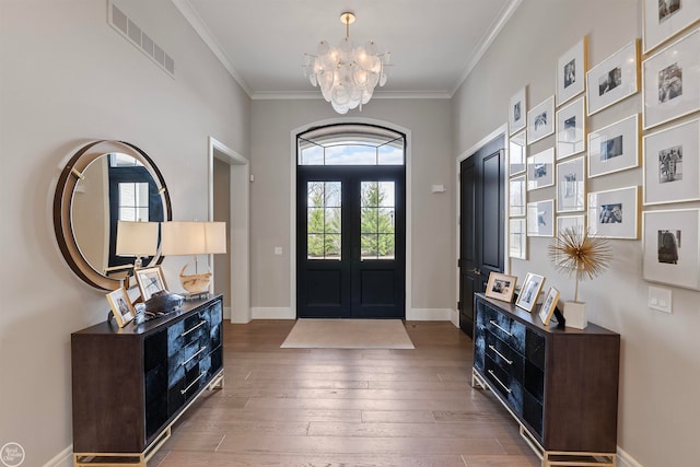 foyer entrance with wood-type flooring, ornamental molding, a chandelier, and french doors