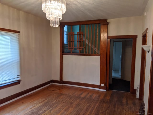 spare room featuring baseboards, a notable chandelier, and wood finished floors