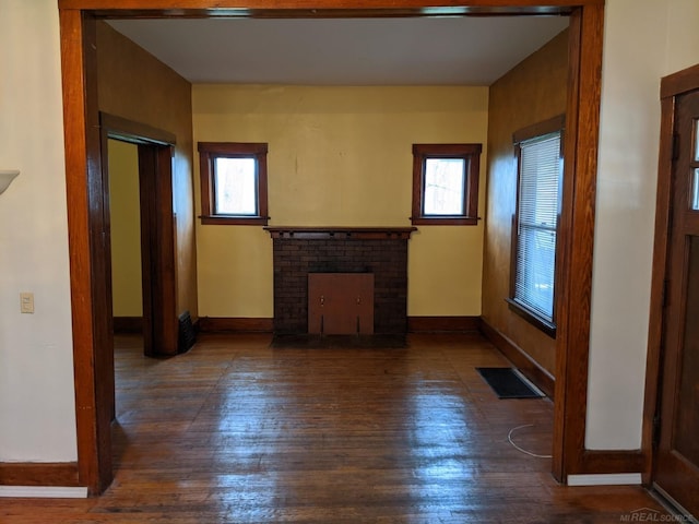 unfurnished living room featuring a wealth of natural light, dark wood-type flooring, and a brick fireplace