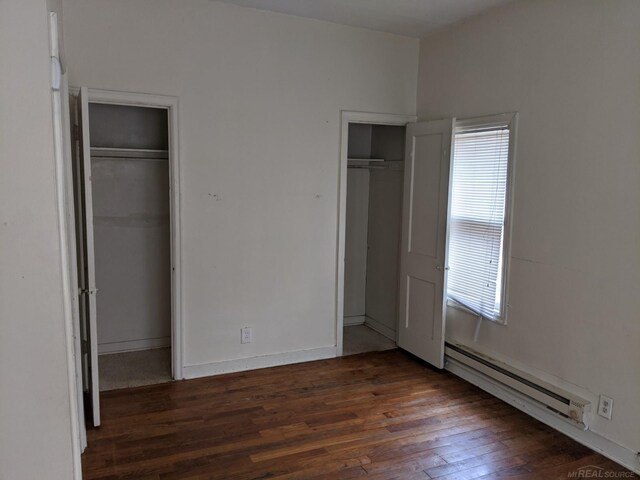 unfurnished bedroom featuring dark wood-type flooring, two closets, and a baseboard heating unit